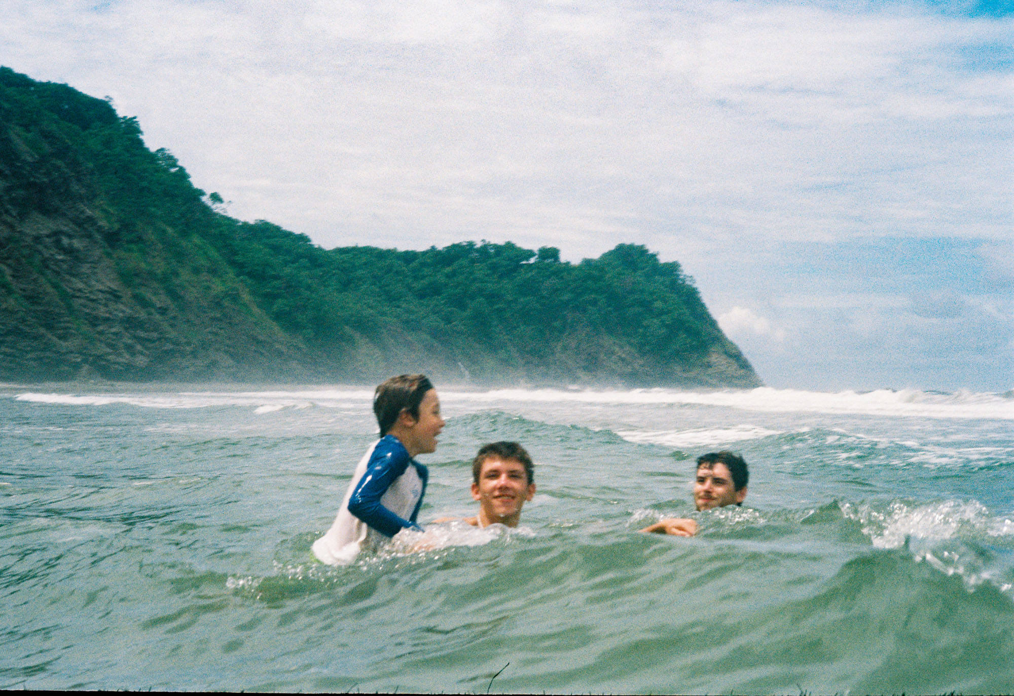 Kids swimming in the waves at Playa Barrigona with jungle headland behind them