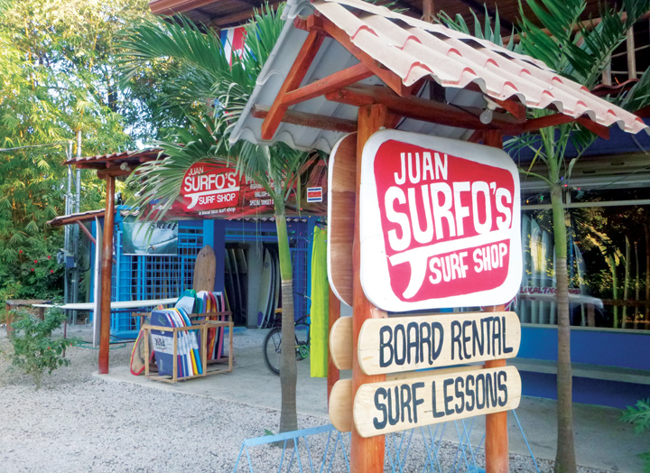 Juan Surfo's Surf Shop storefront in Playa Guiones, Nosara — colorful signs for board rental and surf lessons