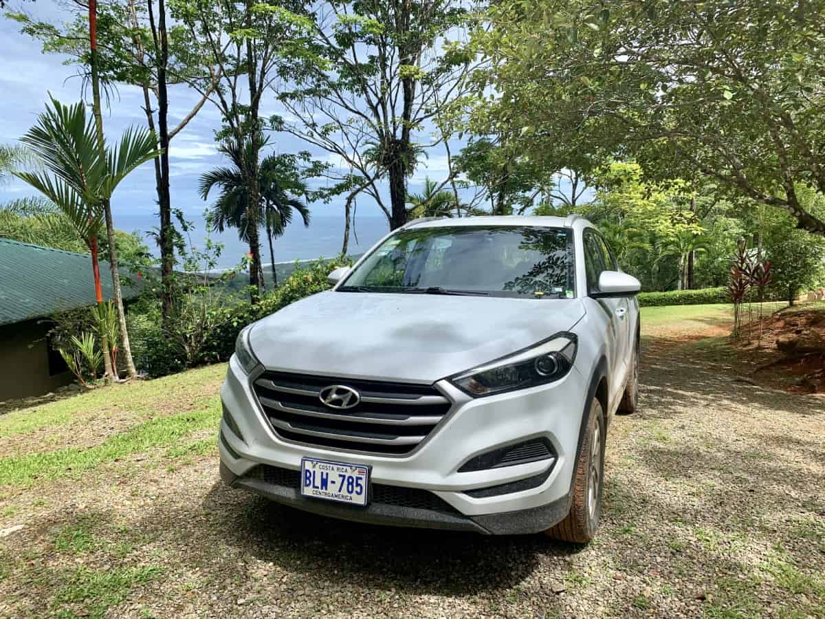 White Hyundai Tucson SUV rental car parked on gravel with ocean views and jungle in Costa Rica