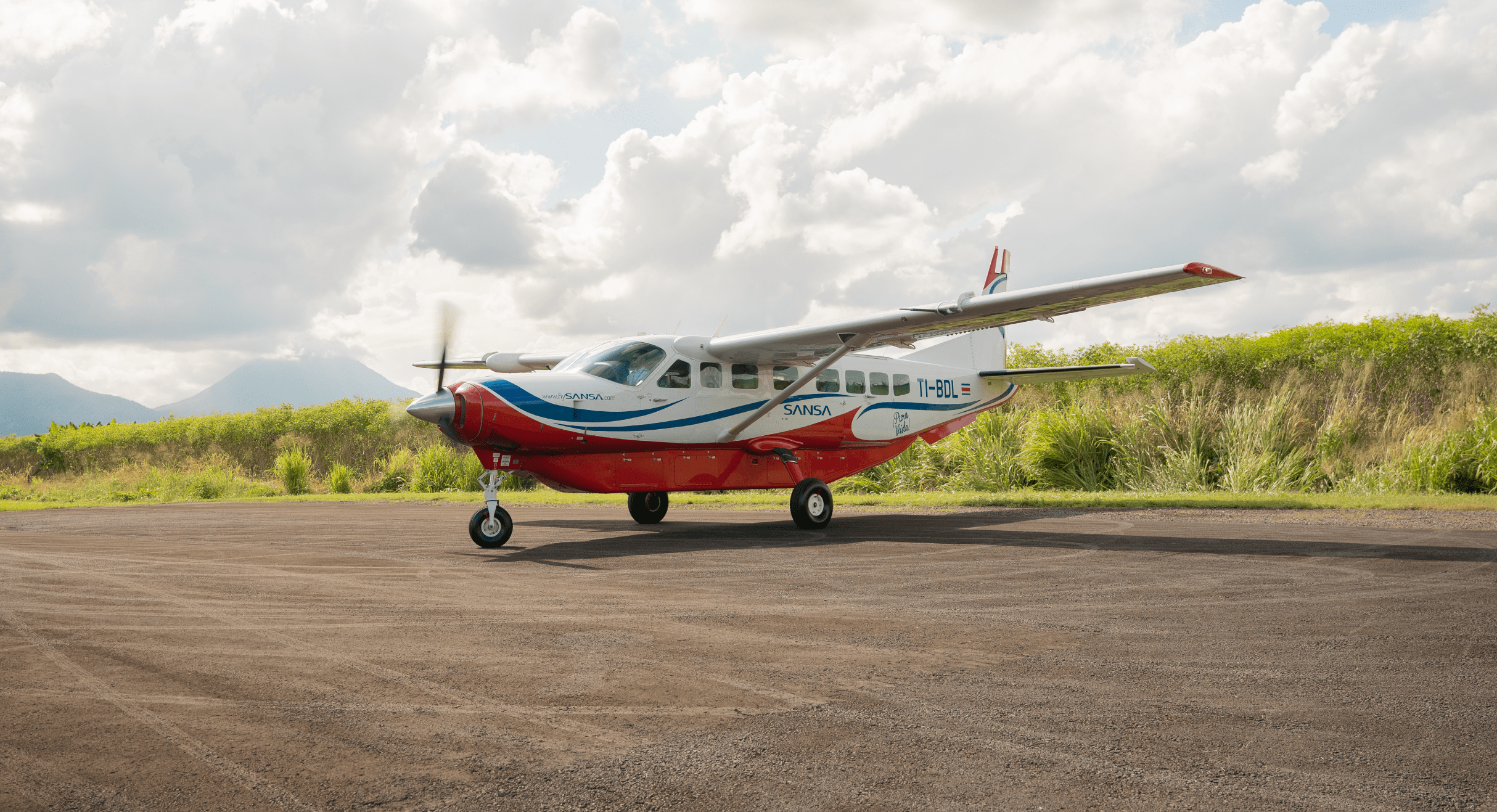 Sansa Airlines Cessna Grand Caravan on a rural Costa Rica airstrip with mountains and dramatic clouds