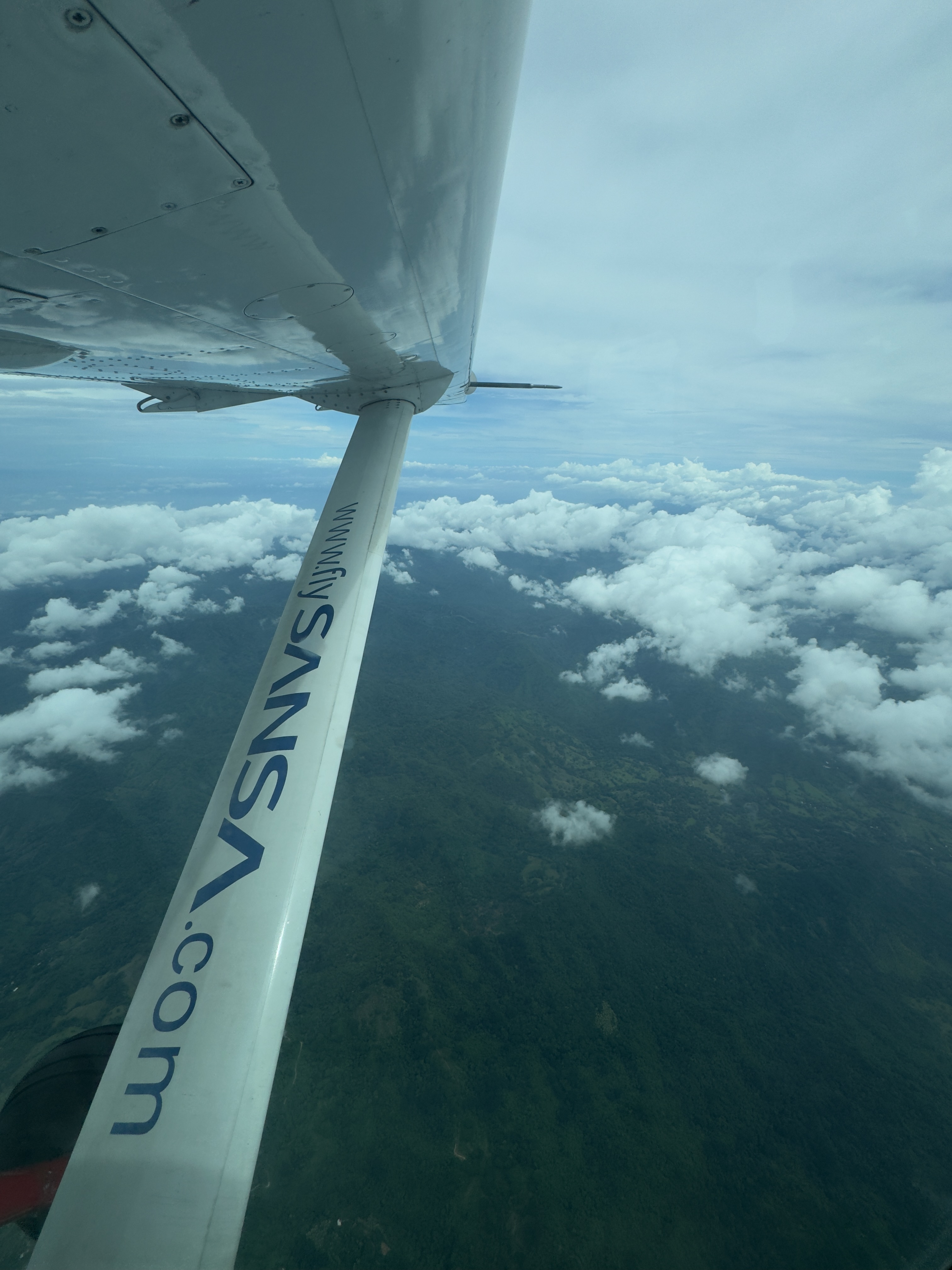View from a Sansa Airlines flight over Costa Rica with flySANSA.com visible on the wing strut and green mountains below