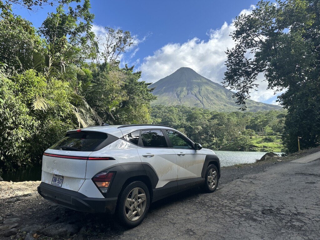 White Hyundai SUV parked on a dirt road with Arenal Volcano rising behind it in Costa Rica