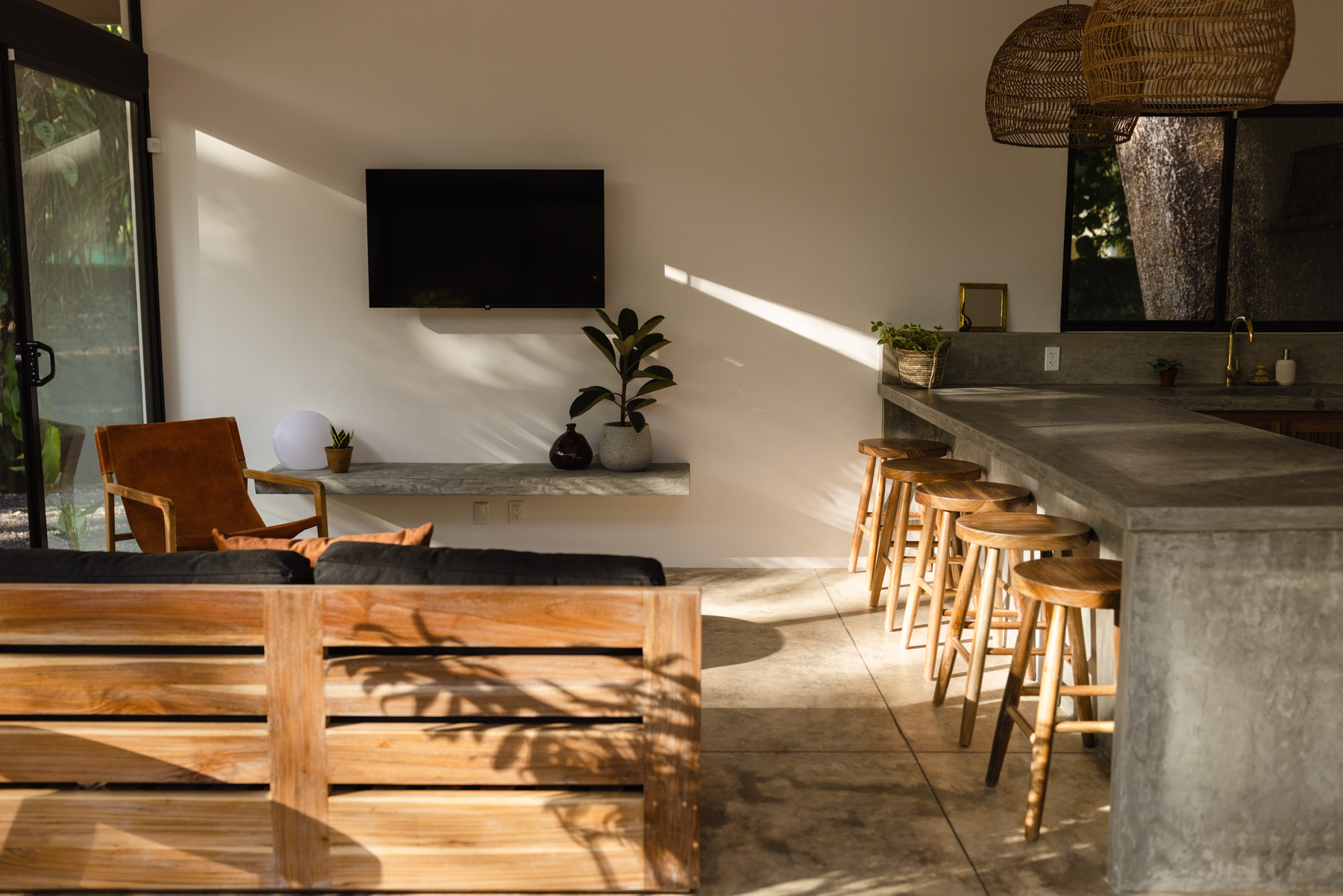Kembar Nosara open-plan living room and kitchen with teak furniture, bar stools, and jungle views through glass doors
