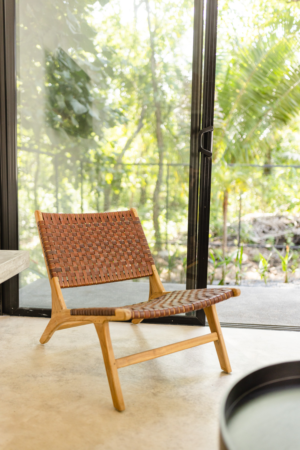 Woven leather chair by floor-to-ceiling glass with jungle bokeh