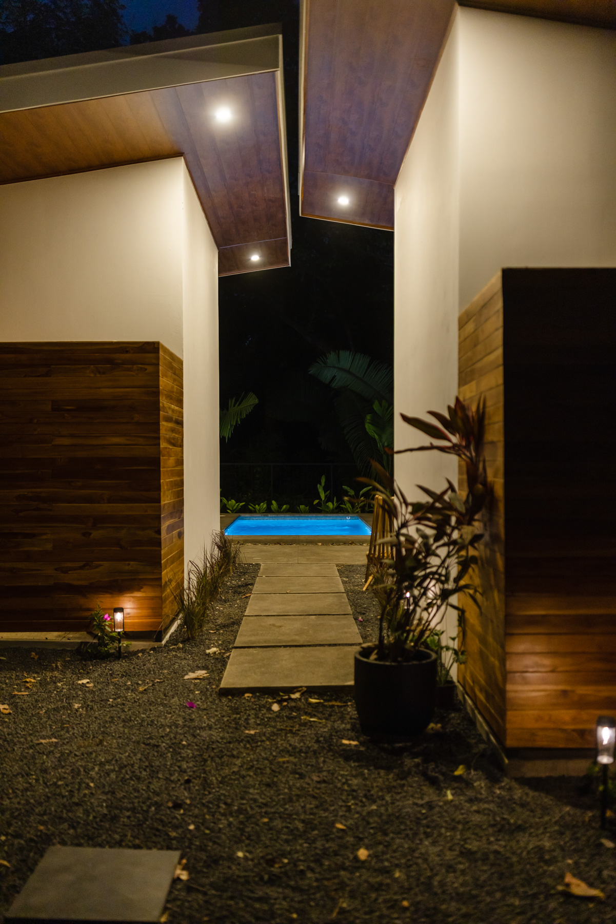 Nighttime walkway between homes with pool glowing in distance